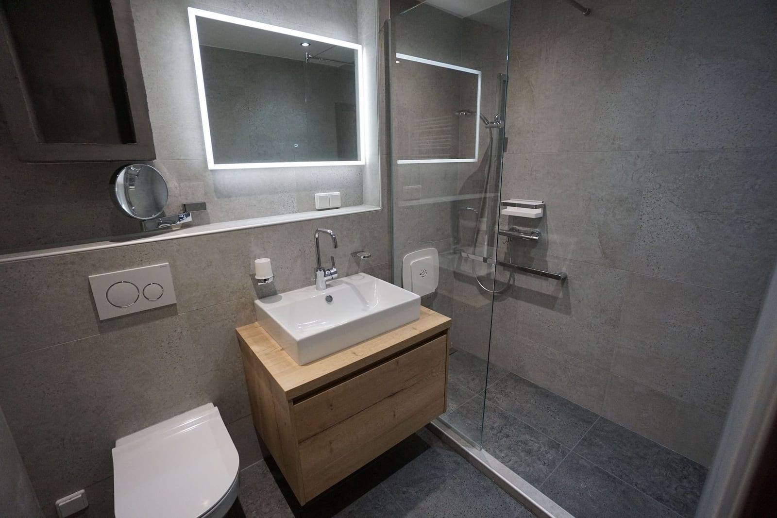 Badezimmer mit grauen Fliesen, Waschtisch und begehbarer Dusche